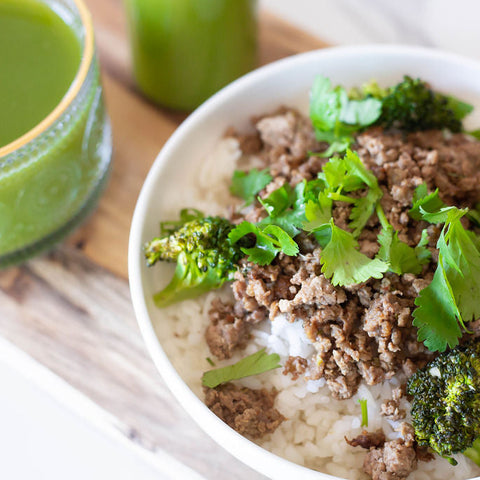 Bowl of food with ground meat, broccoli, and greens on a wooden surface.